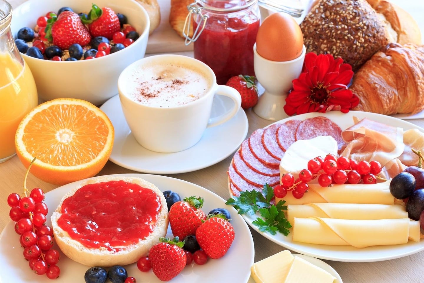 따뜻한 카푸치노 한 잔과 잼을 바른 빵, 신선한 베리류 과일 및 치즈 플레이트가 정갈하게 차려진 호텔 조식 스타일의 상차림입니다.