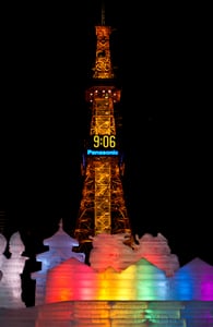 밤하늘 아래 황금빛으로 빛나는 삿포로 TV 타워와 그 앞을 장식한 알록달록한 무지개 빛깔의 얼음 조각들이 어우러진 겨울 축제의 야경입니다.