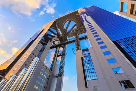 오사카의 랜드마크인 우메다 스카이 빌딩의 거대한 두 타워와 공중 정원 전망대를 연결하는 독특한 철골 구조가 푸른 하늘 아래 웅장하게 펼쳐진 풍경입니다.