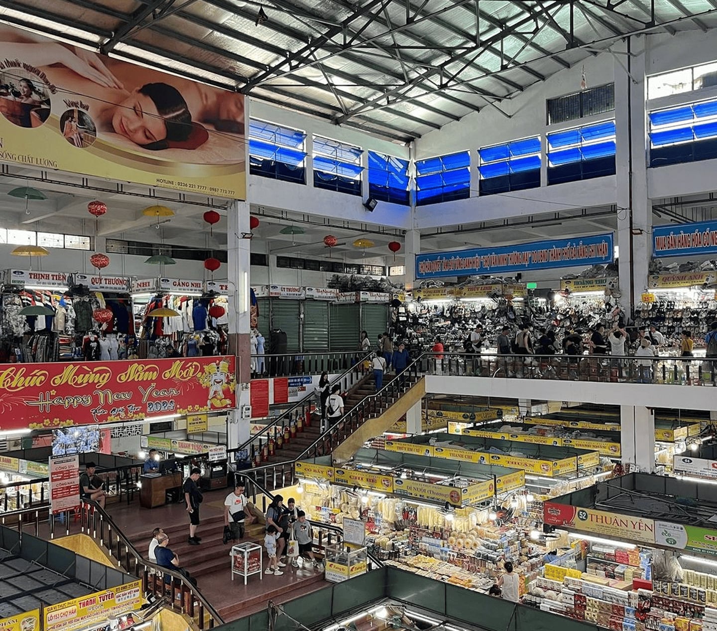 다양한 상점과 인파로 북적이는 베트남 다낭 한 시장의 실내 전경으로 높은 층고와 계단, 화려한 간판들이 어우러진 모습입니다.