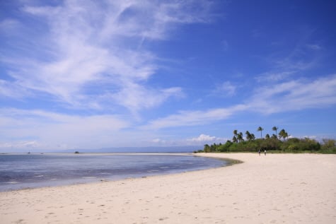 맑고 푸른 하늘과 깃털 같은 구름 아래로 야자수가 우거진 섬과 하얀 모래사장이 어우러진 아름다운 열대 해변의 전경입니다.