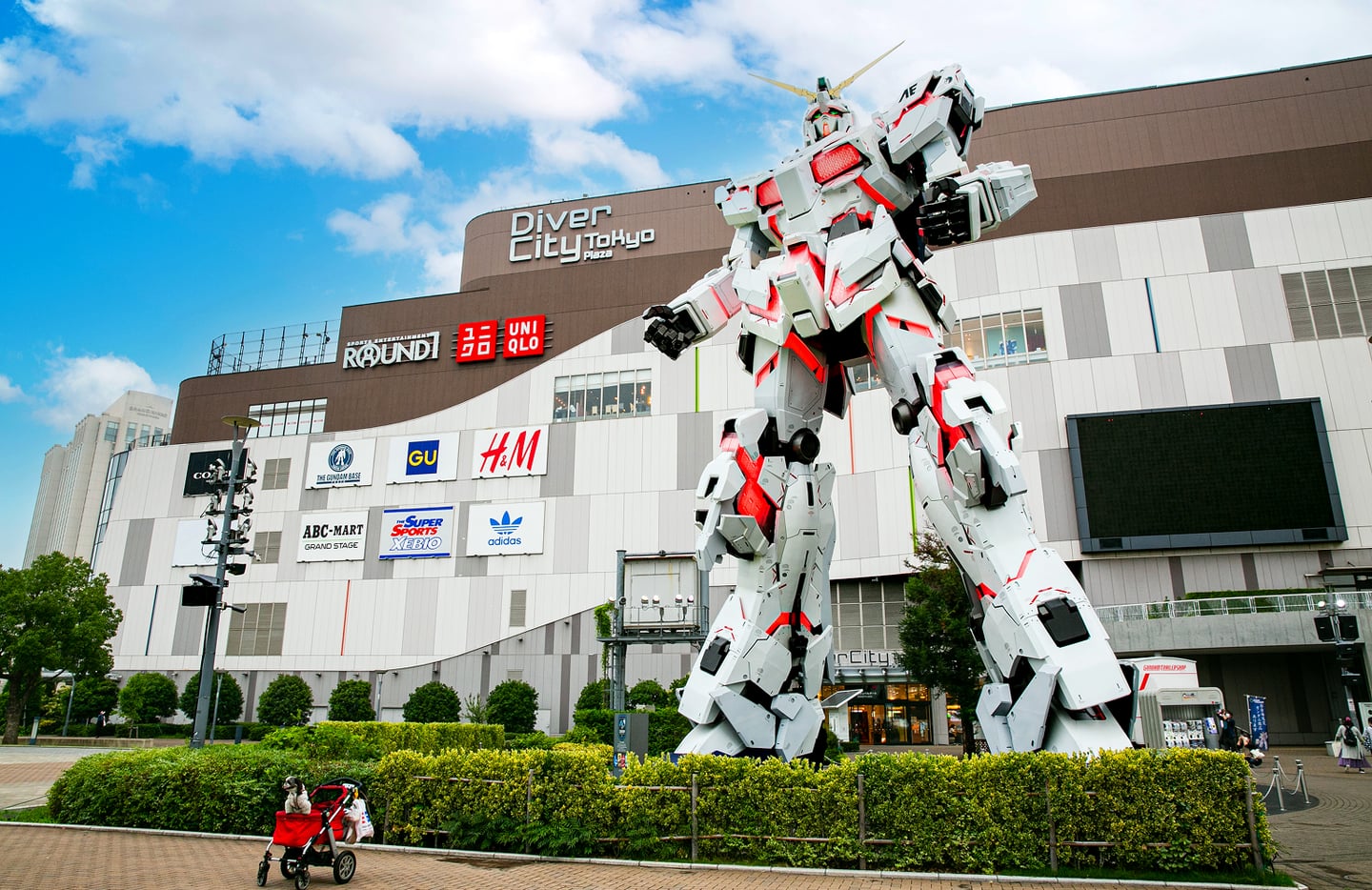 일본 도쿄 오다이바 다이버시티 쇼핑몰 광장에 전시된 거대한 화이트 유니콘 건담 로봇 조형물과 푸른 하늘 아래 도심 풍경입니다.