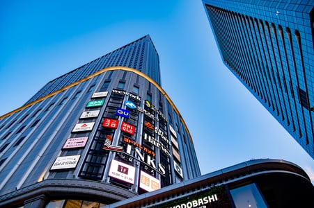 푸른 하늘 아래 유니클로와 요도바시 카메라 등 여러 브랜드 간판이 화려하게 걸려 있는 오사카 링크스 우메다 빌딩의 웅장한 외관입니다.