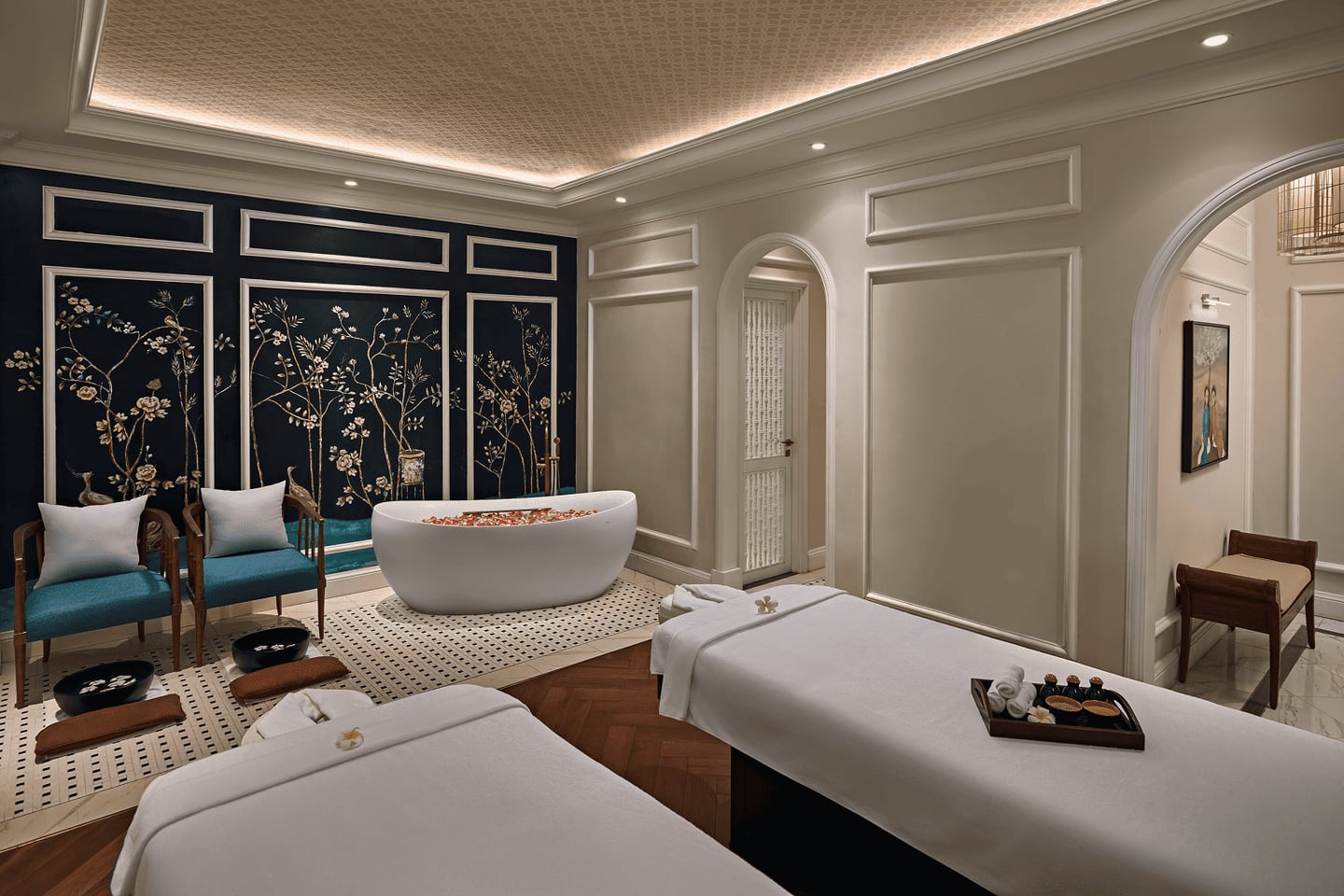 은은한 조명 아래 마사지 베드와 꽃잎 욕조가 갖춰진 럭셔리한 스파 룸에서 평온하고 고급스러운 휴식 분위기가 느껴집니다.