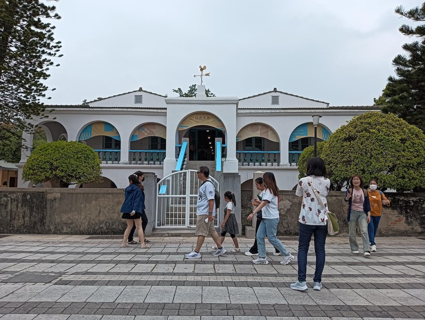 흰색 아치형 입구가 특징인 대만 안평세관 건물 앞에서 다양한 차림의 관광객들이 광장을 가로질러 산책하며 여행을 즐기고 있습니다.