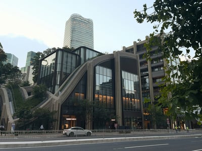 곡선미가 돋보이는 현대적인 디자인의 아자부다이 힐즈 가든 플라자 건물과 그 뒤로 보이는 높은 마천루가 조화를 이루는 도쿄의 도심 풍경입니다.