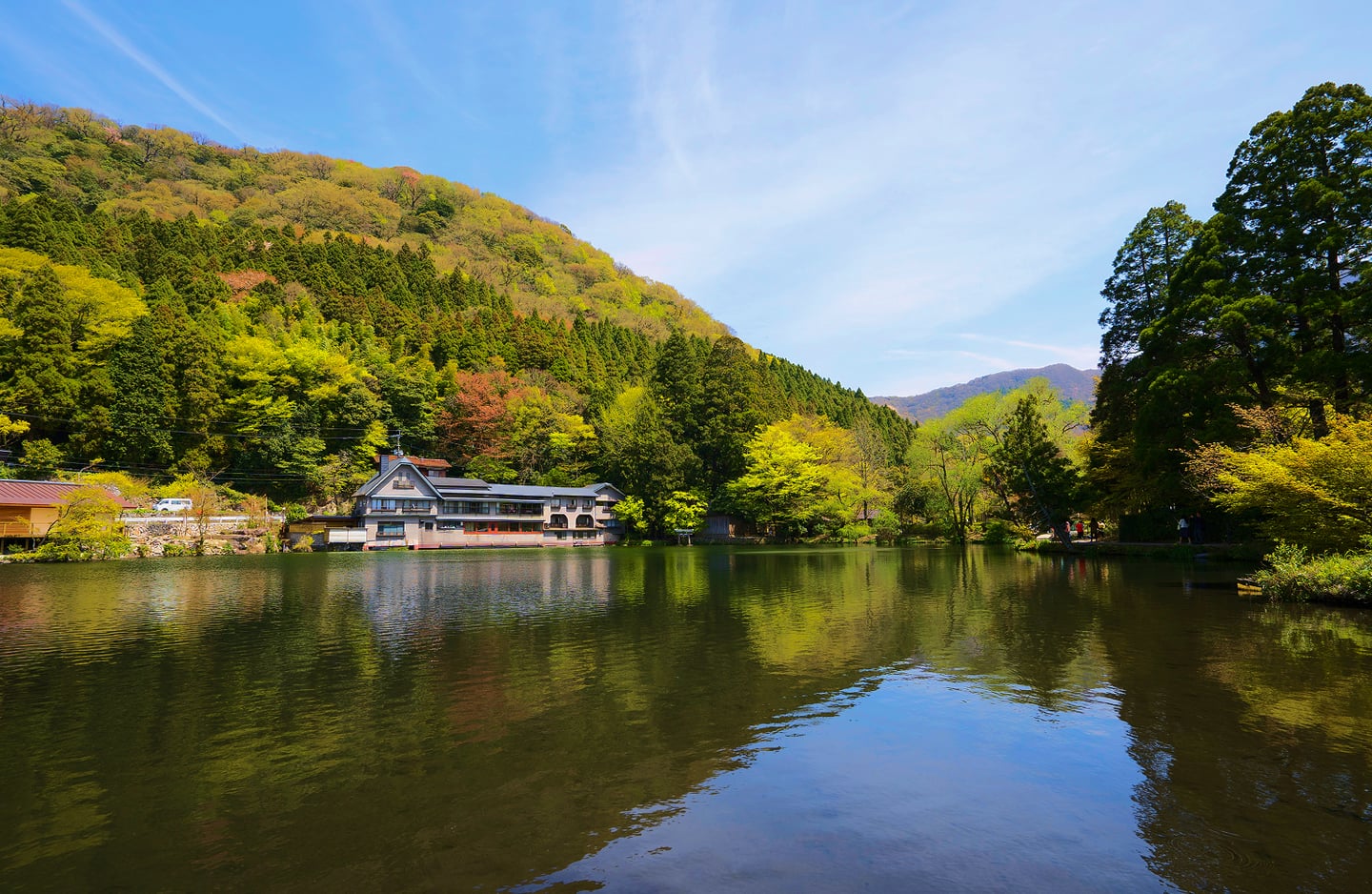 맑고 푸른 하늘 아래 울창한 산과 나무들이 잔잔한 호수면에 그대로 투영되어 평화로운 분위기를 자아내는 일본 유후인 긴린코 호수의 전경입니다.