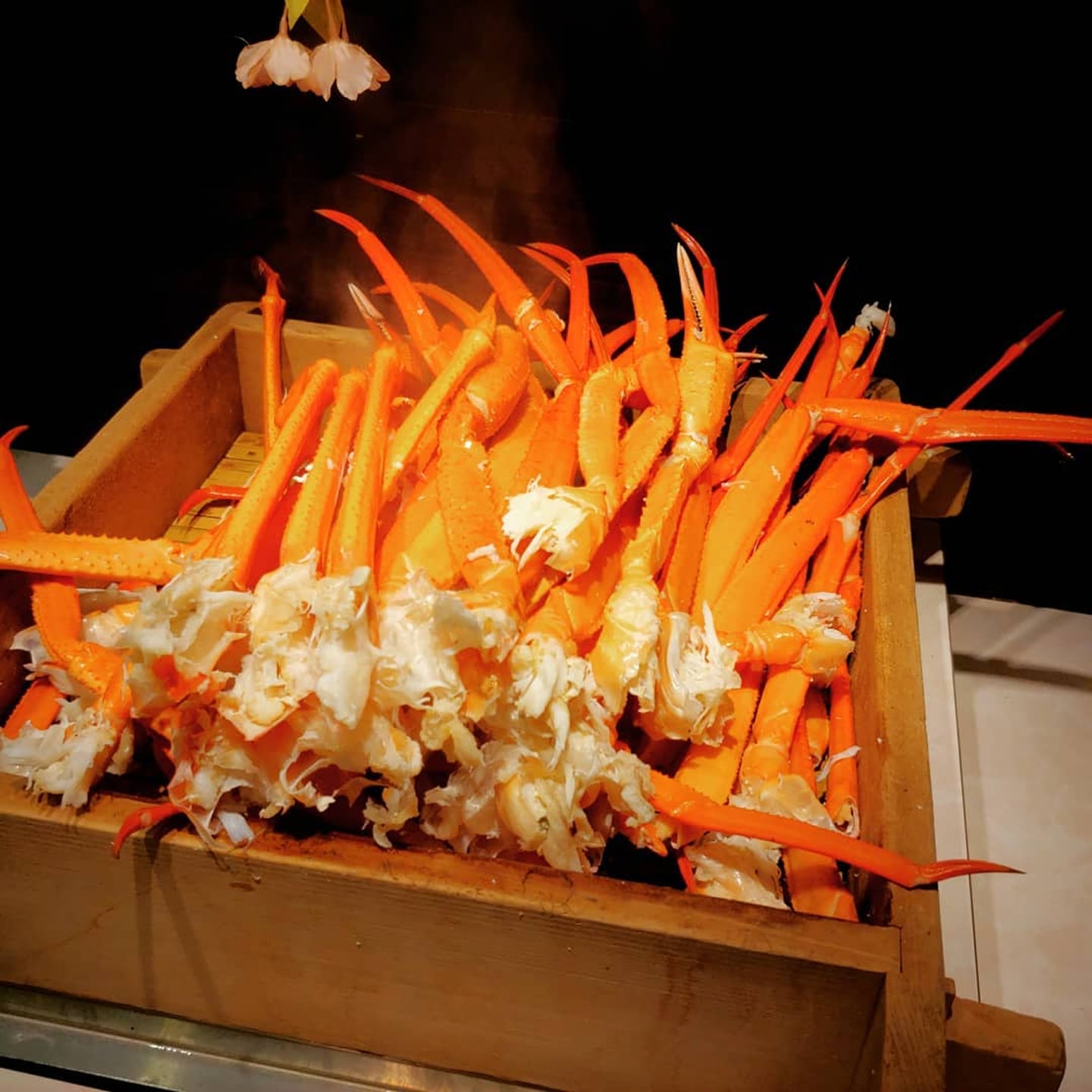 나무 상자 가득 담겨 김이 올라오는 따끈한 대게 다리 찜 요리가 먹음직스러운 비주얼을 뽐내고 있습니다.