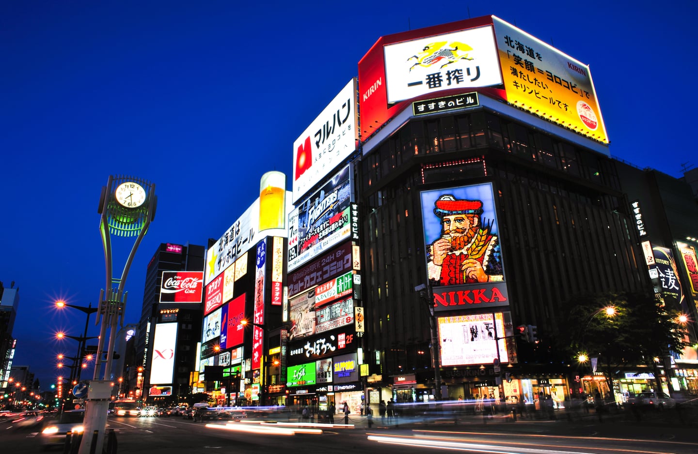 화려한 네온사인과 니카 위스키 광고판이 빛나는 삿포로 스스키노의 밤거리 풍경과 도로 위 자동차 불빛 잔상.