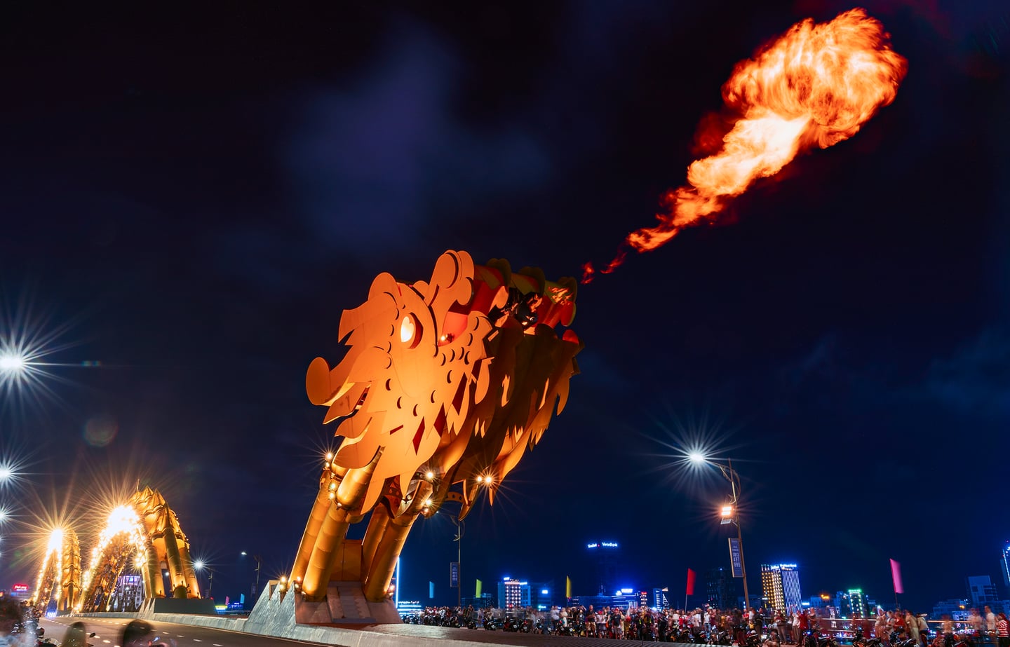 베트남 다낭의 명소인 용다리에서 밤마다 펼쳐지는 화려한 불꽃 쇼의 모습으로, 황금색 용 조형물이 입에서 거대한 불길을 내뿜으며 도시의 밤을 밝히고 있습니다.