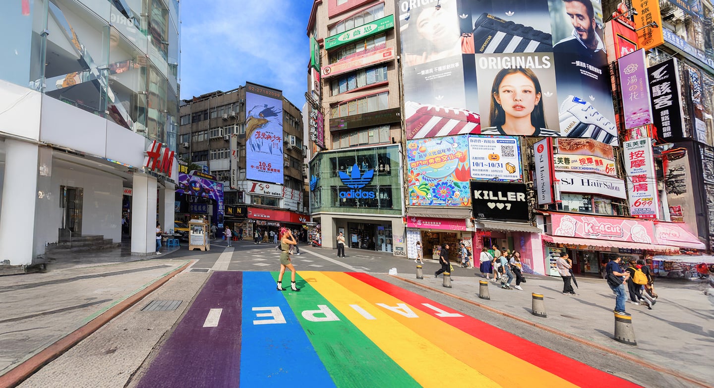 타이베이 시먼딩의 번화한 거리 풍경으로 바닥에 그려진 선명한 무지개색 타이베이 로고와 주변의 화려한 대형 광고판들이 활기찬 도시 분위기를 자아냅니다.