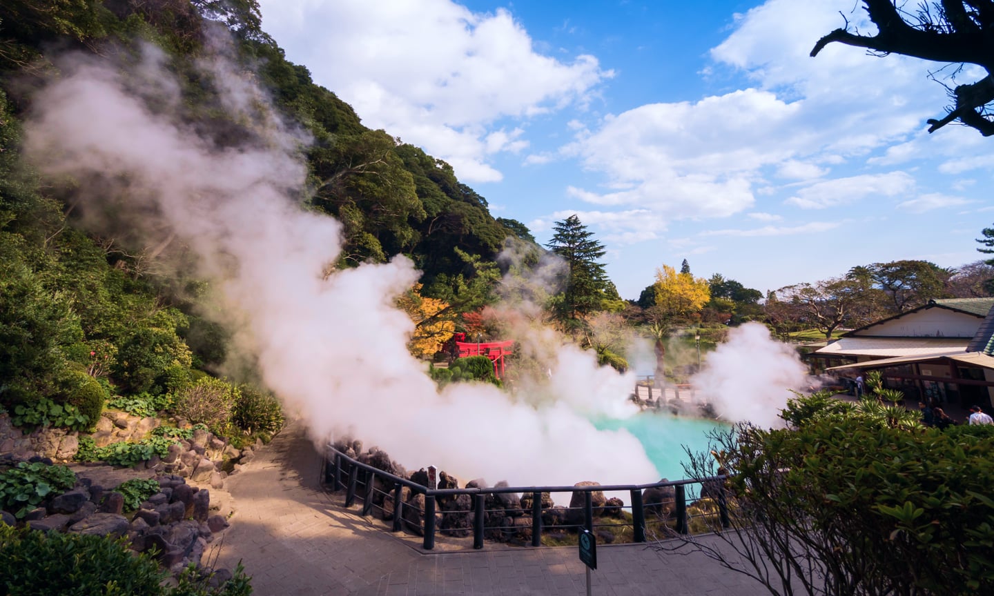 에메랄드빛 온천수에서 솟아오르는 하얀 증기와 주변의 푸른 숲, 붉은 도리이가 조화를 이루는 일본 벳푸 우미지옥의 평화로운 풍경입니다.