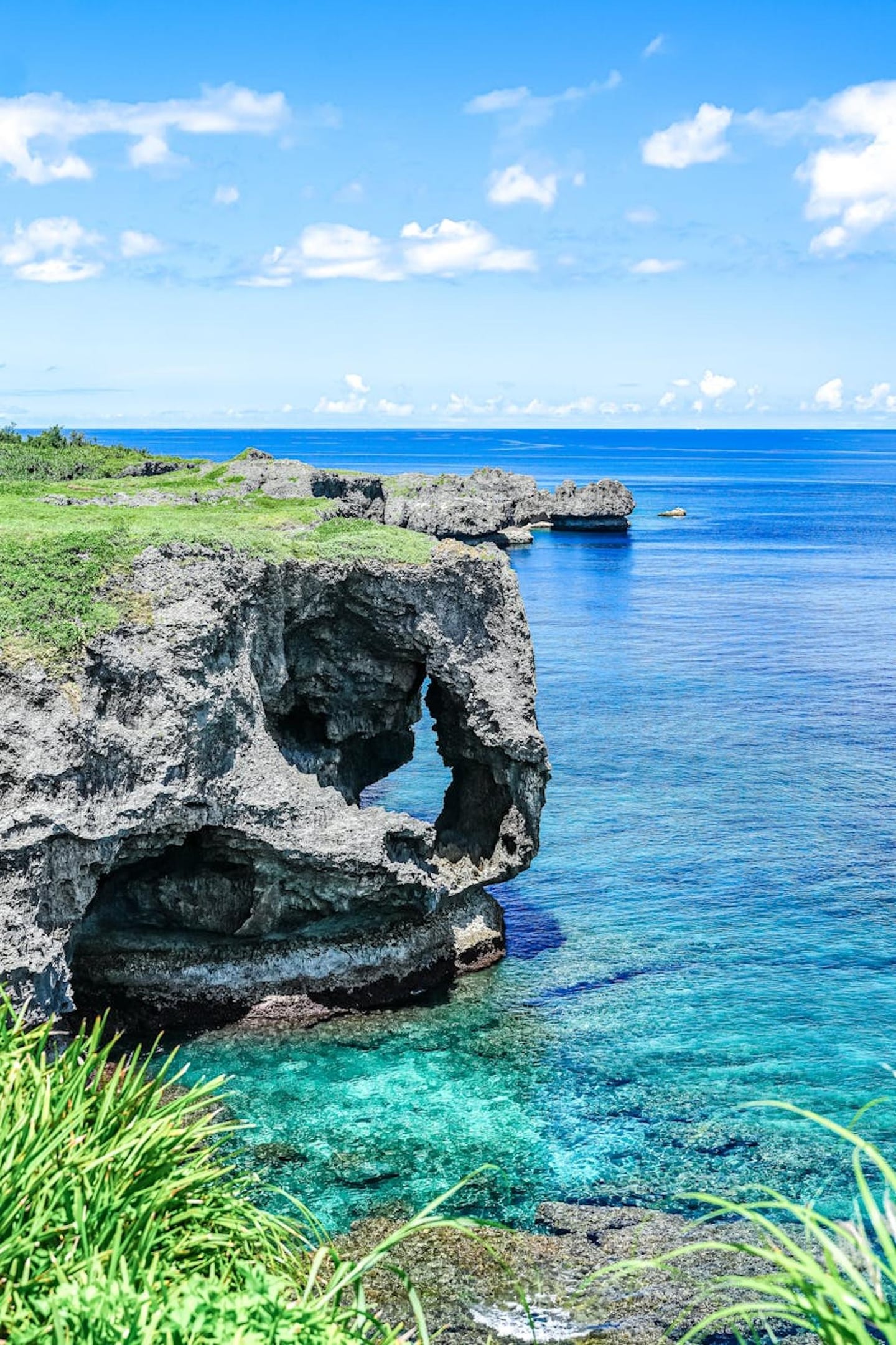 맑고 푸른 하늘 아래 코끼리 형상을 한 거대한 해안 절벽과 투명한 에메랄드빛 바다가 어우러진 오키나와 만좌모의 전경입니다.