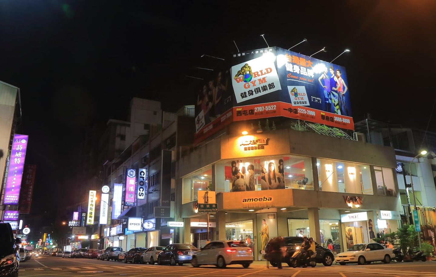 화려한 조명의 대형 광고판과 다양한 상점들이 즐비한 대만 도심의 밤거리에서 차들이 도로를 따라 이동하는 모습입니다.