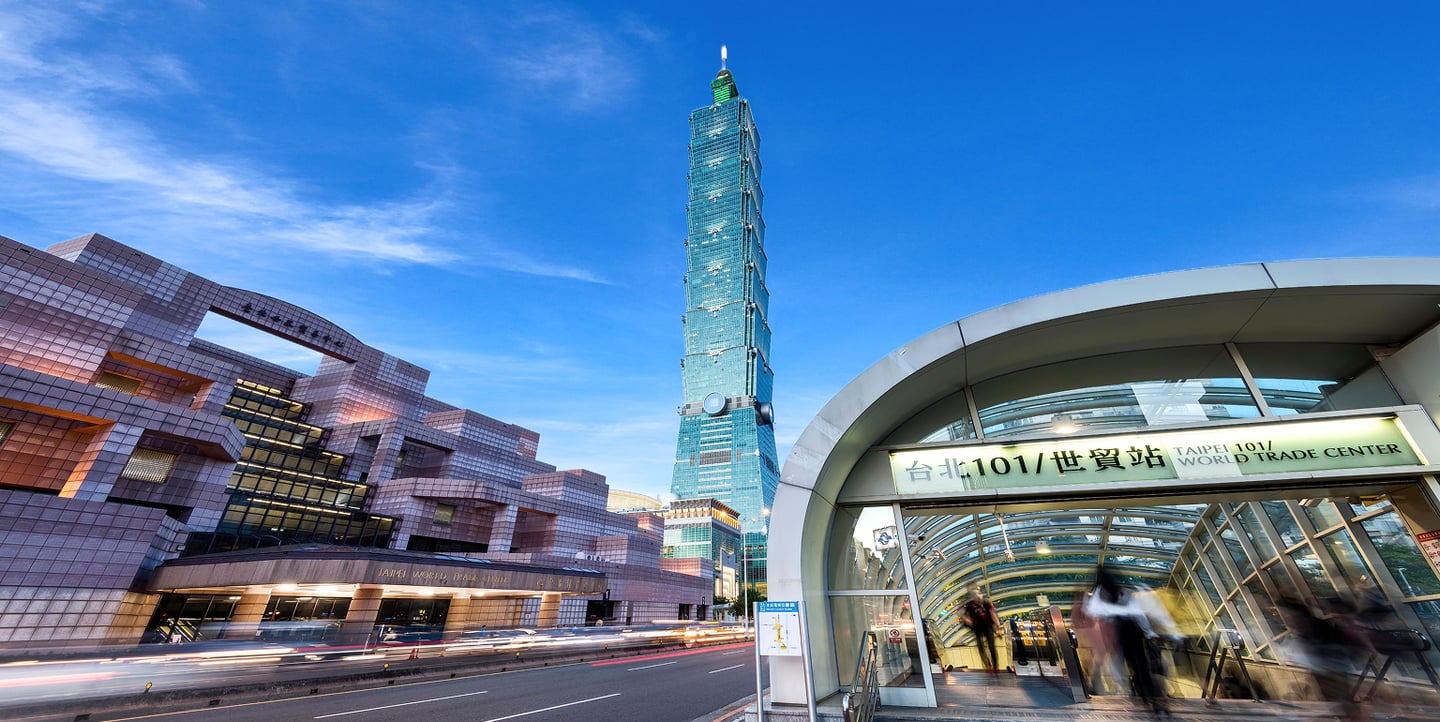대만 타이베이 101 빌딩이 보이는 도심 거리에서 지하철역 입구와 세계무역센터 건물이 푸른 하늘과 조화를 이루는 풍경입니다.
