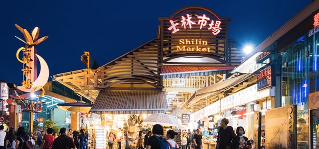 화려한 붉은색 네온사인 간판이 빛나는 대만 타이베이 스린 야시장 입구에서 수많은 관광객들이 밤거리를 거닐며 쇼핑을 즐기는 모습입니다.