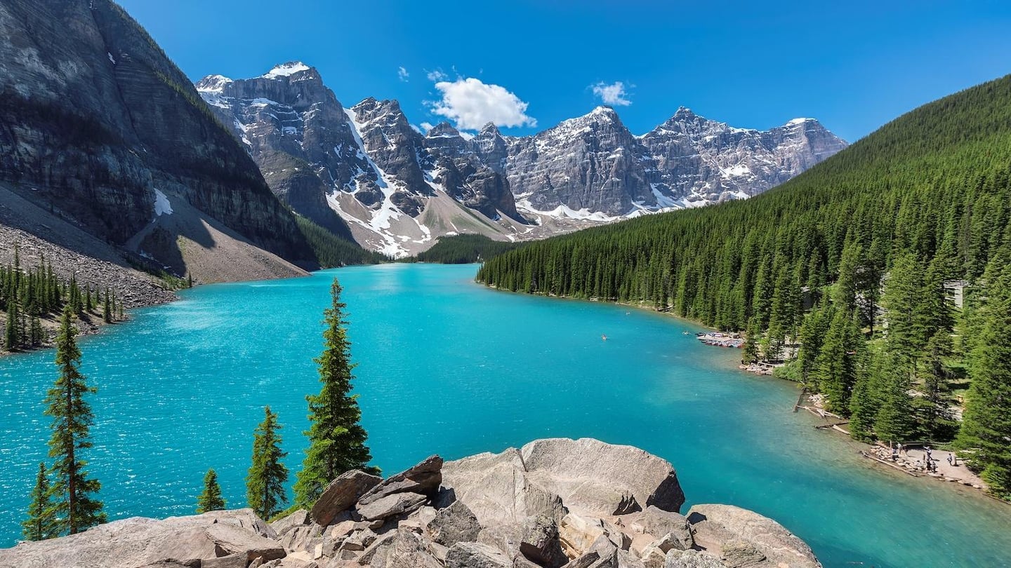 눈 덮인 봉우리와 울창한 숲이 감싸고 있는 신비로운 에메랄드빛 호수가 바위 언덕 너머로 펼쳐지는 캐나다 밴프 국립공원의 풍경입니다.