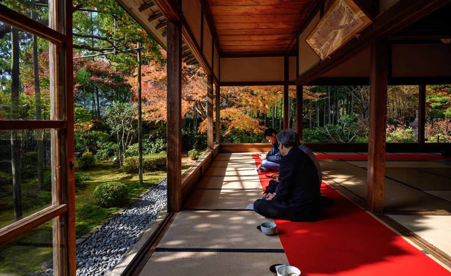 가을 단풍이 아름답게 물든 일본 전통 가옥의 다다미 방에서 사람들이 정원을 바라보며 휴식을 취하는 평온한 풍경입니다.
