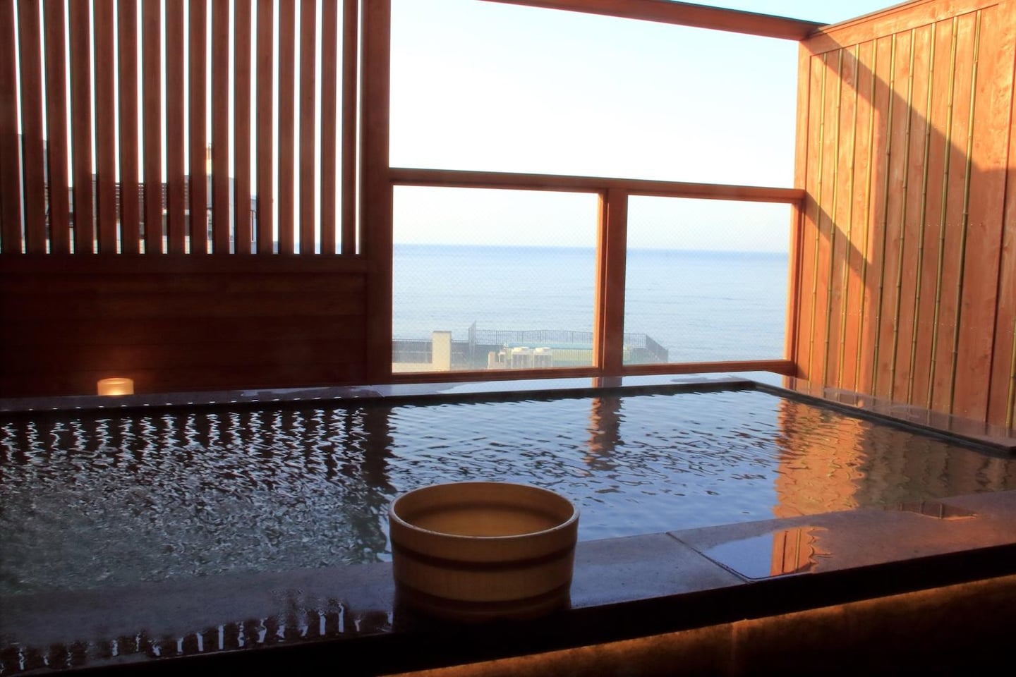 탁 트인 바다 전망을 감상하며 온천욕을 즐길 수 있는 목재 인테리어의 노천탕과 물 위에 띄워진 나무 대야의 모습입니다.