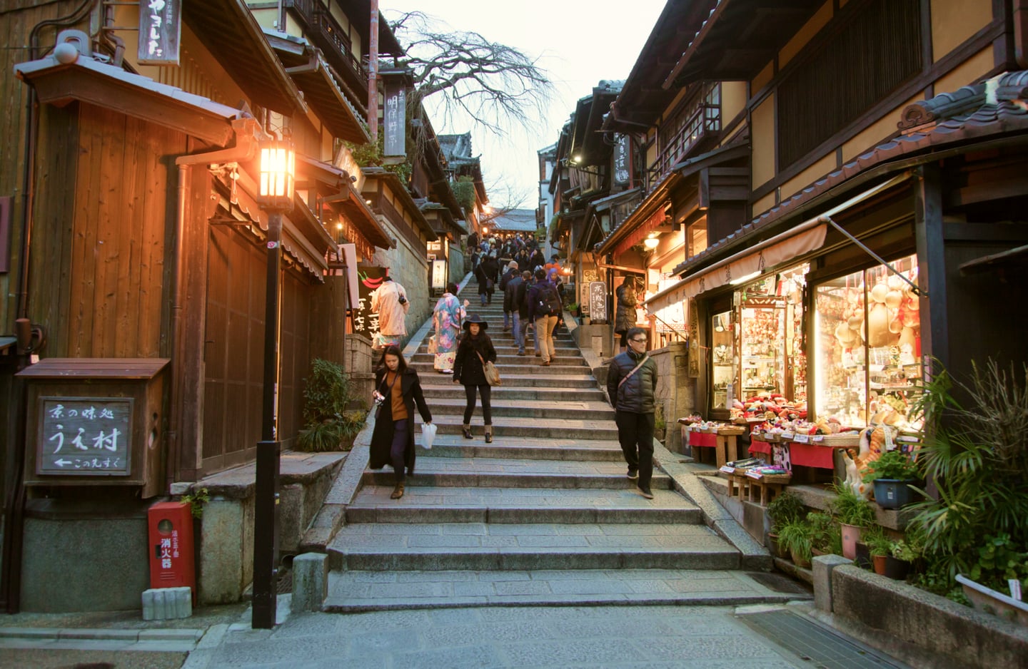 교토의 유서 깊은 산넨자카 돌계단 거리를 따라 관광객들이 이동하고 있으며 주변에는 전통 목조 가옥과 기념품 상점들이 줄지어 있습니다.