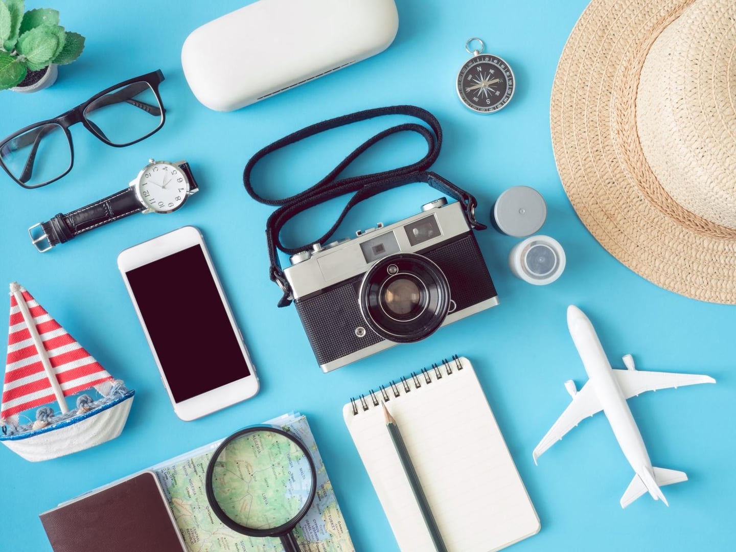 푸른 배경 위에 놓인 빈티지 카메라와 스마트폰, 지도, 여권, 비행기 모형 등 다채로운 여행 소품들이 조화롭게 어우러진 여행 준비 컨셉 사진입니다.
