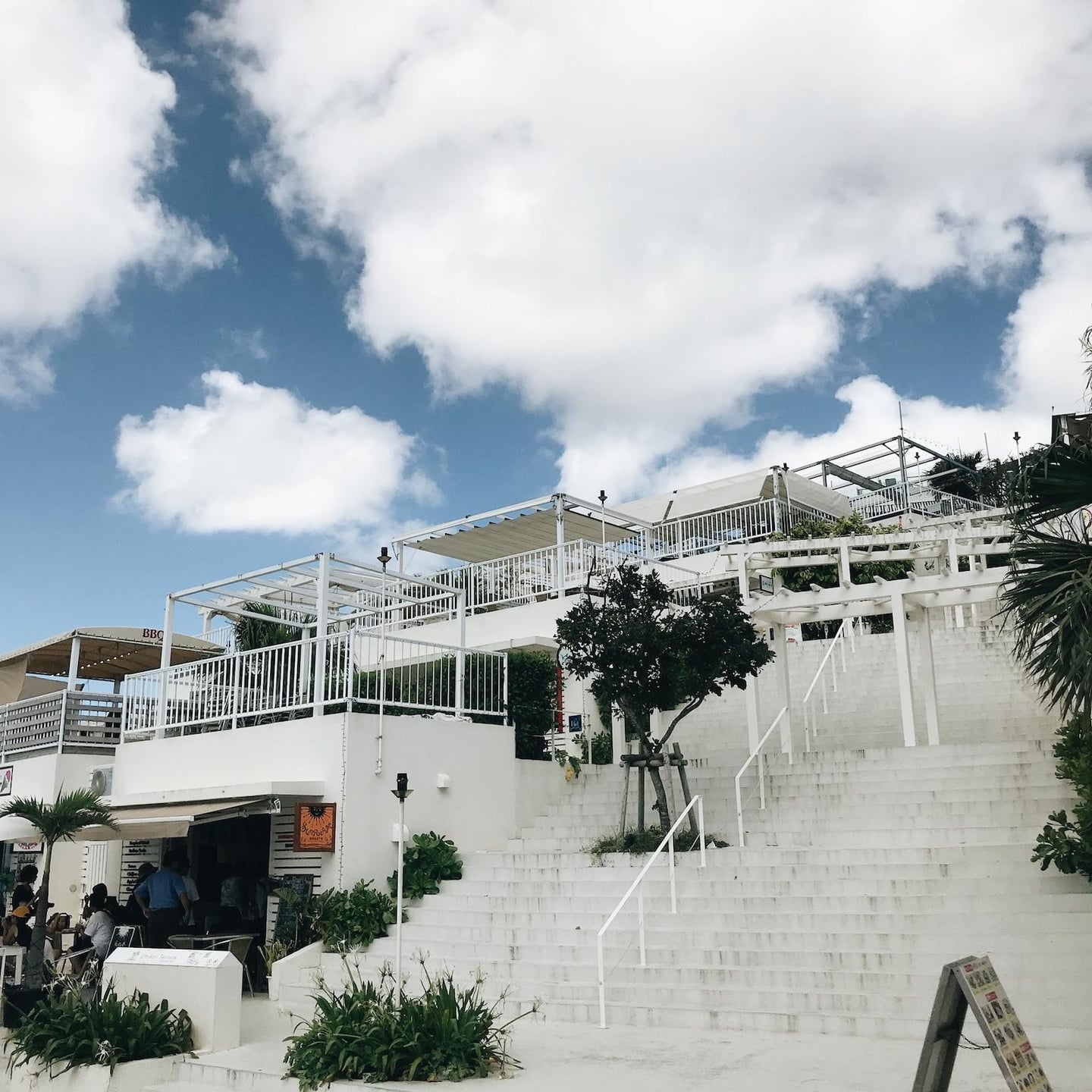 맑고 푸른 하늘을 배경으로 하얀색 계단과 테라스 건물이 층층이 쌓여 있는 오키나와 우미카지 테라스의 평화로운 전경입니다.