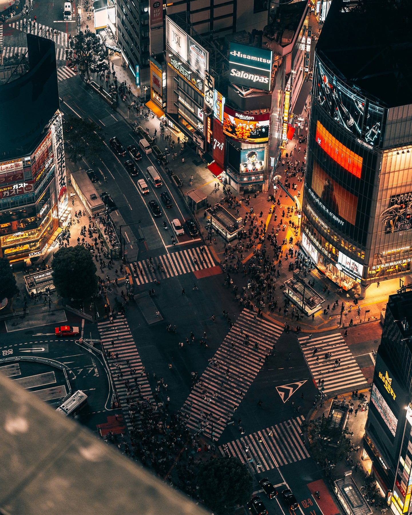 도쿄 시부야의 화려한 밤거리 풍경으로, 수많은 사람들이 횡단보도를 가로지르고 밝은 전광판이 빛나는 고층 빌딩들이 교차로를 둘러싸고 있는 역동적인 모습입니다.