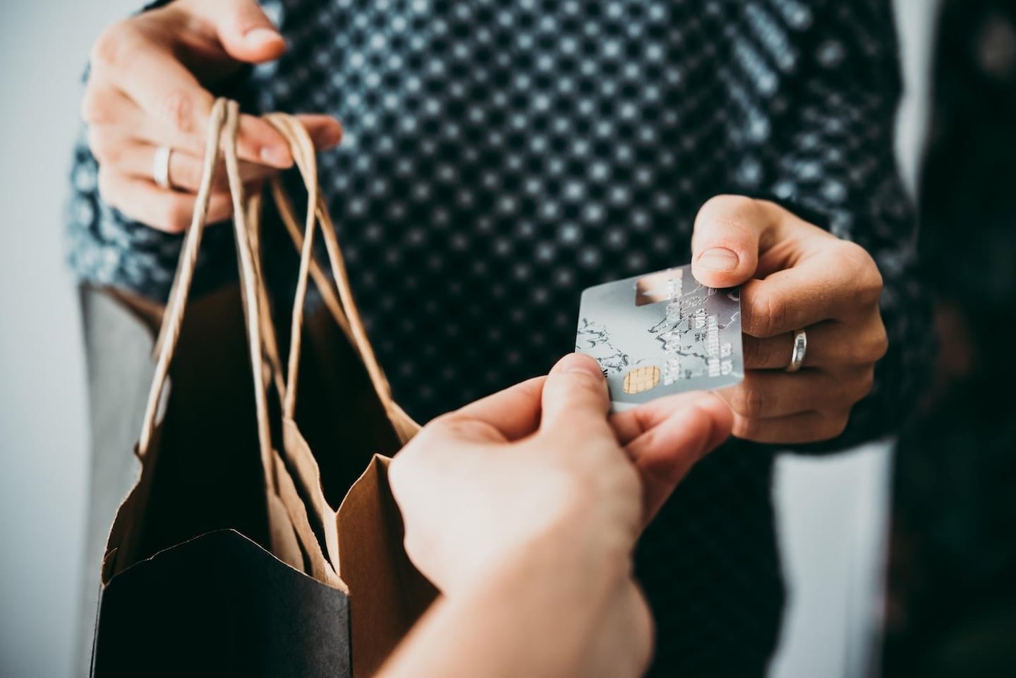 쇼핑백을 든 손과 결제를 위해 신용카드를 건네는 손이 클로즈업된 모습으로 소비와 구매의 순간을 생생하게 보여줍니다.