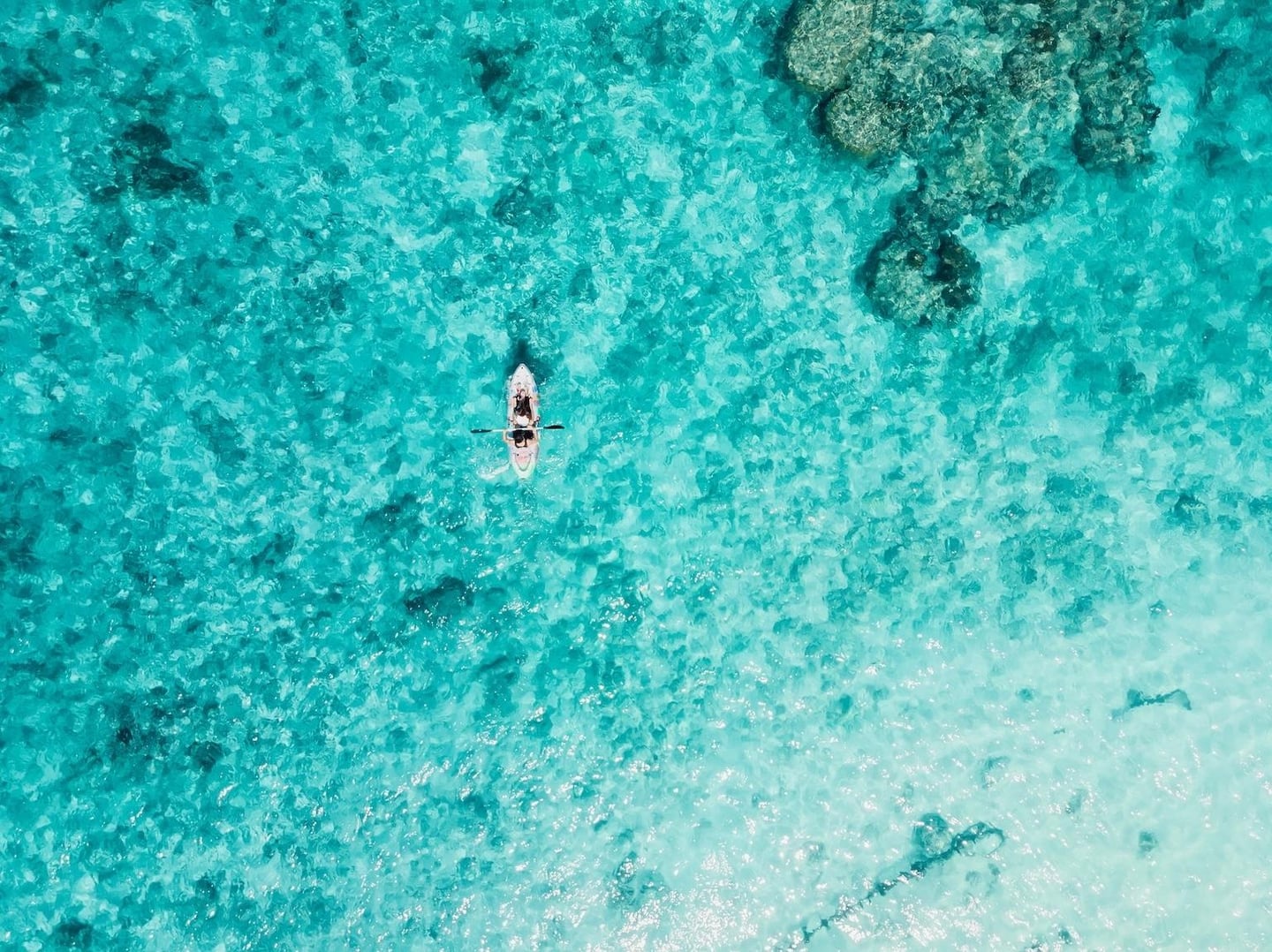 투명한 에메랄드빛 바다 위에서 카약을 타고 여유롭게 노를 젓는 사람들의 모습을 담은 평화로운 항공 뷰 이미지입니다.