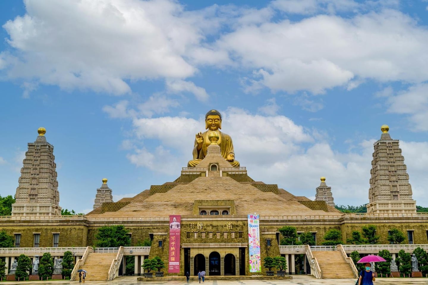대만 가오슝 불광산 불타기념관의 웅장한 황금 불상과 계단식 사원 건물이 푸른 하늘과 구름을 배경으로 펼쳐진 풍경입니다.