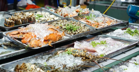 동남아시아 야시장 가판대 위에 얼음을 가득 채운 쟁반마다 게와 랍스터, 조개류 등 싱싱한 해산물이 먹음직스럽게 진열되어 있는 모습입니다.