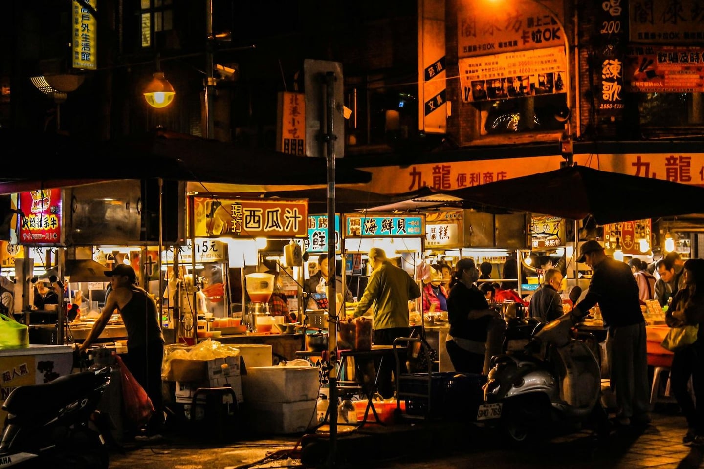 화려한 네온사인과 한자 간판이 즐비한 대만 야시장에서 상인들이 음식을 준비하고 사람들이 모여 있는 활기찬 밤거리의 모습입니다.