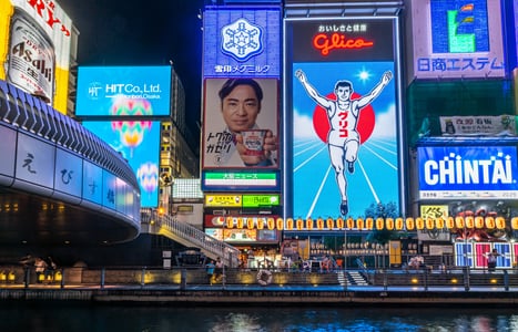 오사카 도톤보리 운하를 배경으로 화려하게 빛나는 글리코상 전광판과 다양한 상업 광고들이 어우러진 일본의 역동적인 야경 모습입니다.