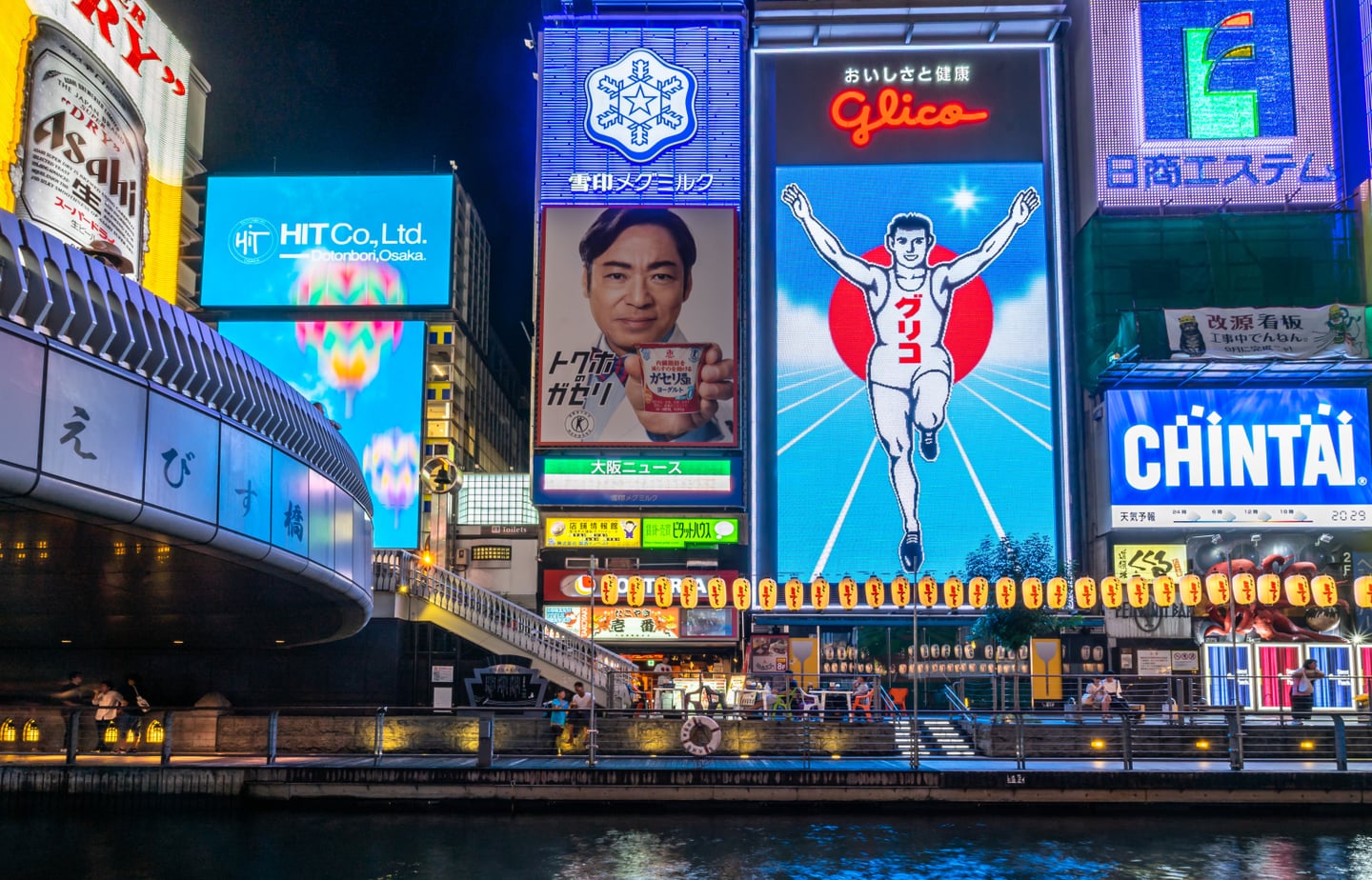 오사카 도톤보리 운하를 배경으로 화려하게 빛나는 글리코상 전광판과 다양한 상업 광고들이 어우러진 일본의 역동적인 야경 모습입니다.