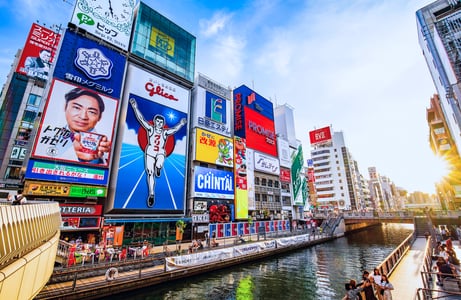 오사카 도톤보리 운하를 따라 늘어선 글리코상과 화려한 대형 광고판들이 푸른 하늘과 어우러져 활기찬 일본 도심의 낮 풍경을 보여줍니다.
