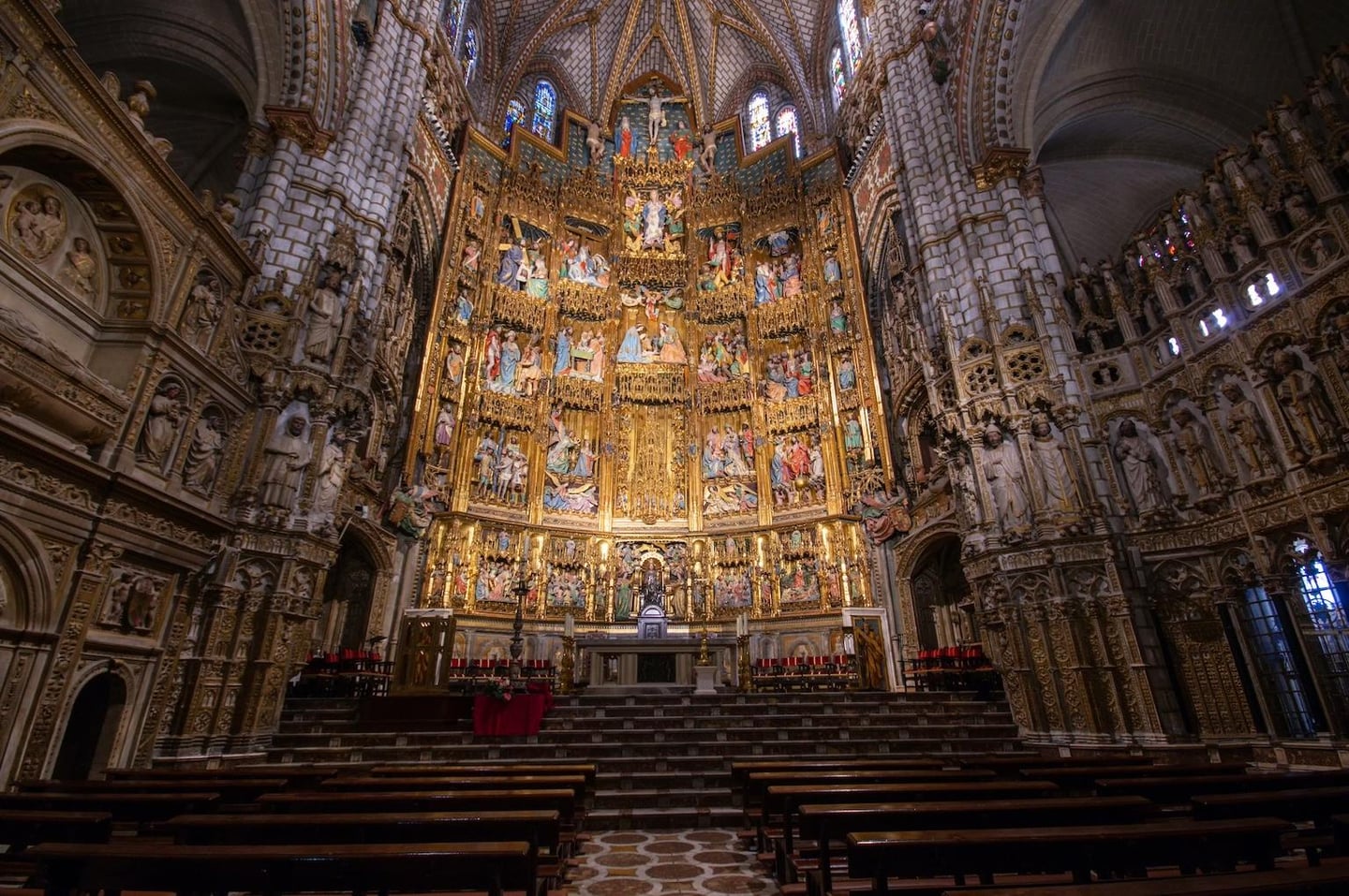화려한 금색 조각과 성화로 장식된 거대한 제단이 있는 성당 내부 전경으로, 높은 천장과 정교한 건축 양식이 돋보이는 역사적인 예배당의 모습입니다.