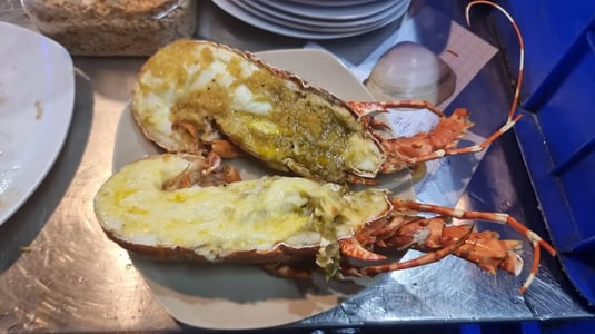 먹음직스럽게 구워진 랍스터 두 마리가 반으로 나뉘어 치즈와 소스가 토핑된 채 접시에 담겨 있는 모습입니다.