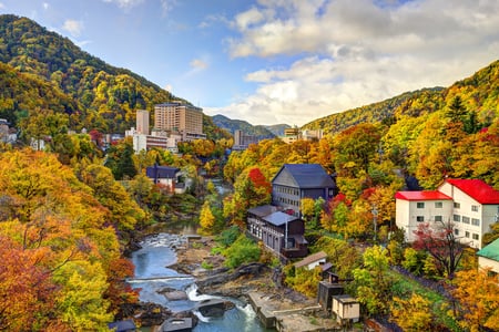 가을 단풍이 화려하게 물든 산과 계곡을 따라 조성된 일본 조잔케이 온천 마을의 평화로운 전경이 펼쳐져 있습니다.