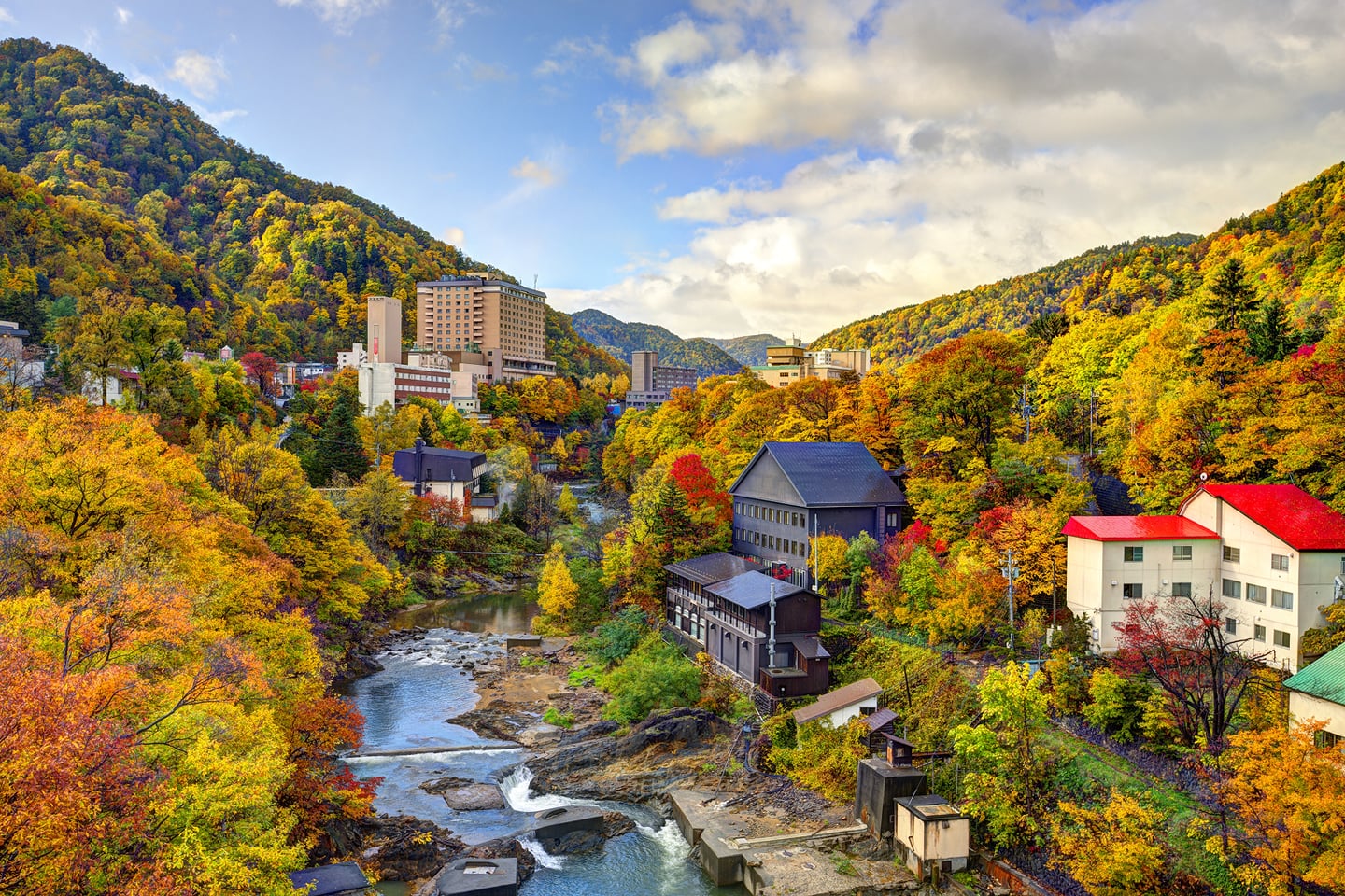 가을 단풍이 화려하게 물든 산과 계곡을 따라 조성된 일본 조잔케이 온천 마을의 평화로운 전경이 펼쳐져 있습니다.