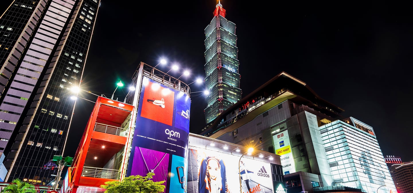 화려한 조명이 켜진 타이베이 101 빌딩과 대형 광고판이 가득한 번화가의 역동적인 밤 풍경을 담은 로우 앵글 사진입니다.