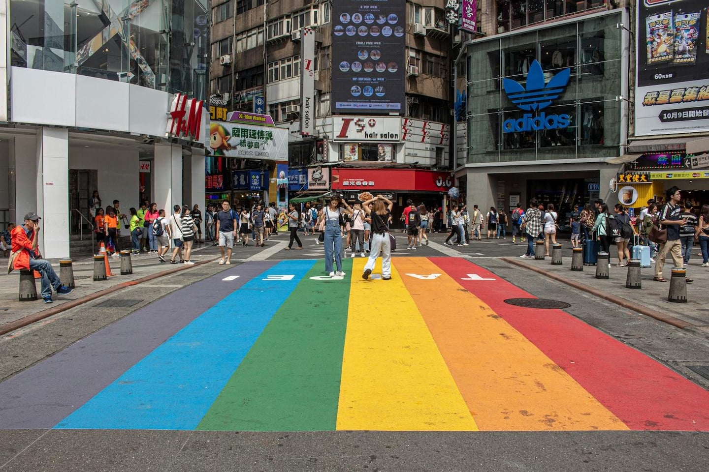 타이베이 시먼딩의 상징적인 무지개 횡단보도 위에서 사람들이 사진을 찍고 활기찬 쇼핑 거리를 즐기는 풍경입니다.