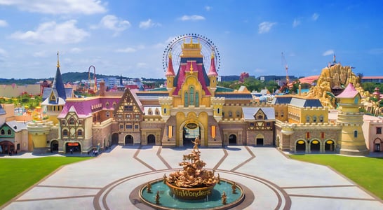 맑은 날씨 속 빈원더스 테마파크의 화려한 성과 대관람차, 그리고 광장 중앙의 황금빛 분수대가 어우러진 이국적인 풍경입니다.