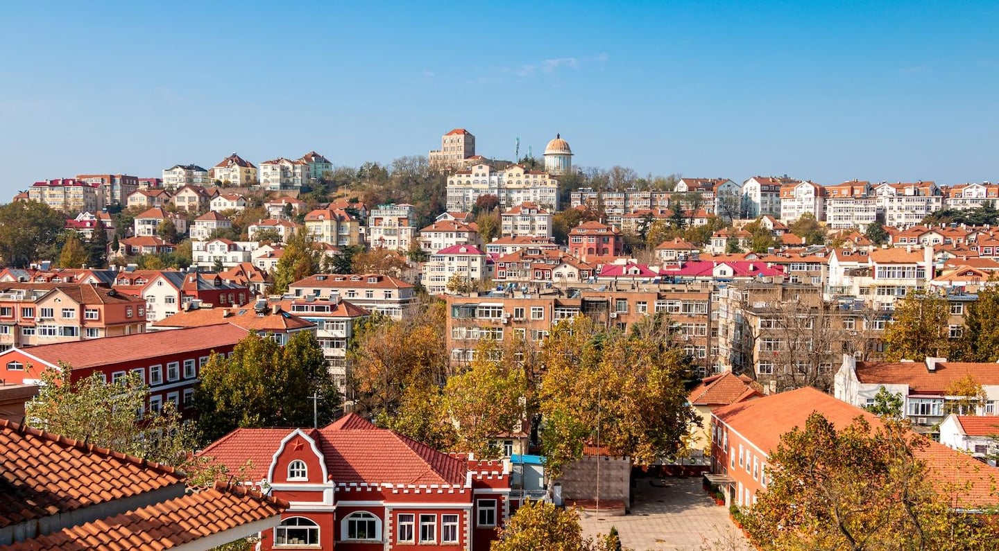 맑은 하늘 아래 붉은 기와지붕과 유럽풍 건축물들이 조화를 이루며 언덕 위로 펼쳐진 중국 칭다오 시내의 아름다운 풍경입니다.