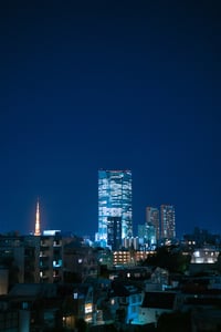 짙은 푸른 밤하늘을 배경으로 밝게 빛나는 고층 빌딩들과 붉은 조명의 도쿄 타워가 어우러진 일본 도쿄의 아름다운 도시 야경 모습입니다.