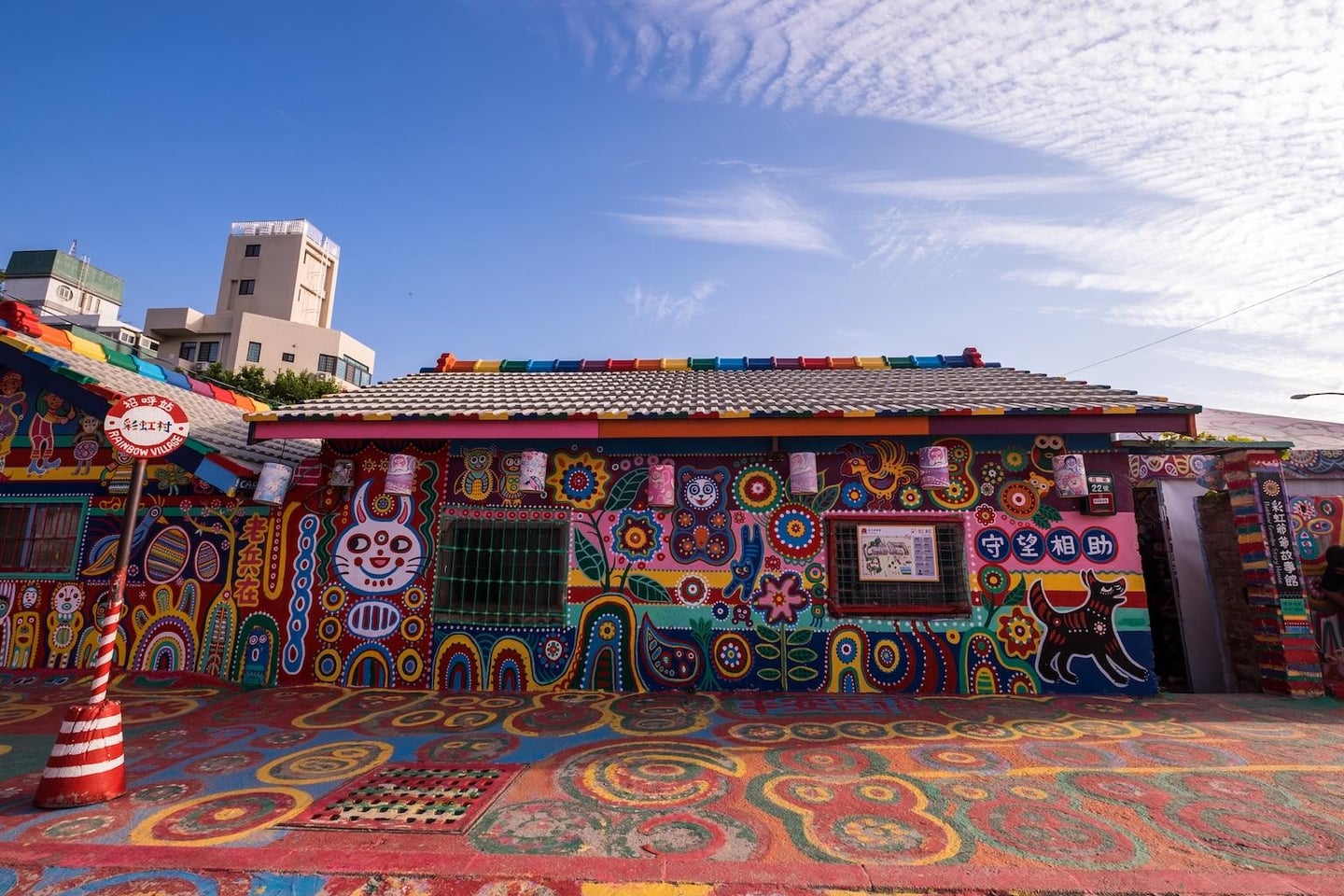 푸른 하늘 아래 화려한 원색의 벽화와 캐릭터들로 장식된 대만 타이중 무지개 마을의 이색적인 건물 외관과 바닥 풍경입니다.