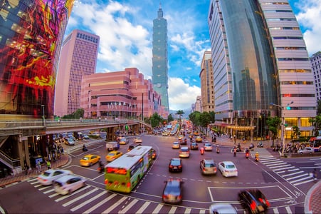푸른 하늘 아래 타이베이 101 타워가 보이는 번화한 도심 교차로에서 수많은 차량이 이동하며 활기찬 도시의 일상을 보여주는 풍경입니다.