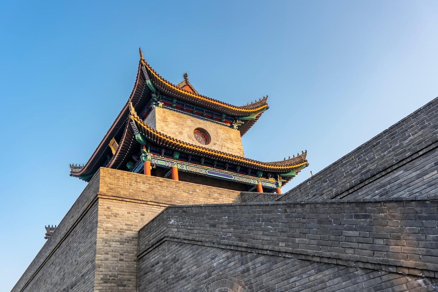 맑고 푸른 하늘 아래 웅장하게 솟아있는 중국 전통 성벽과 화려한 단청 장식이 돋보이는 다층 누각의 고풍스러운 풍경입니다.