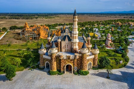 웅장한 첨탑을 가진 중세 유럽 스타일의 성 건물과 그 뒤로 펼쳐진 롤러코스터 및 테마파크의 다채로운 풍경이 조화를 이루는 모습입니다.