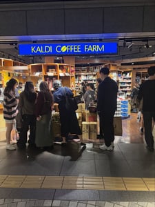 일본의 유명 식료품점인 칼디 커피 팜 매장 입구에서 여러 명의 손님들이 진열된 상품을 구경하며 쇼핑을 즐기는 모습입니다.