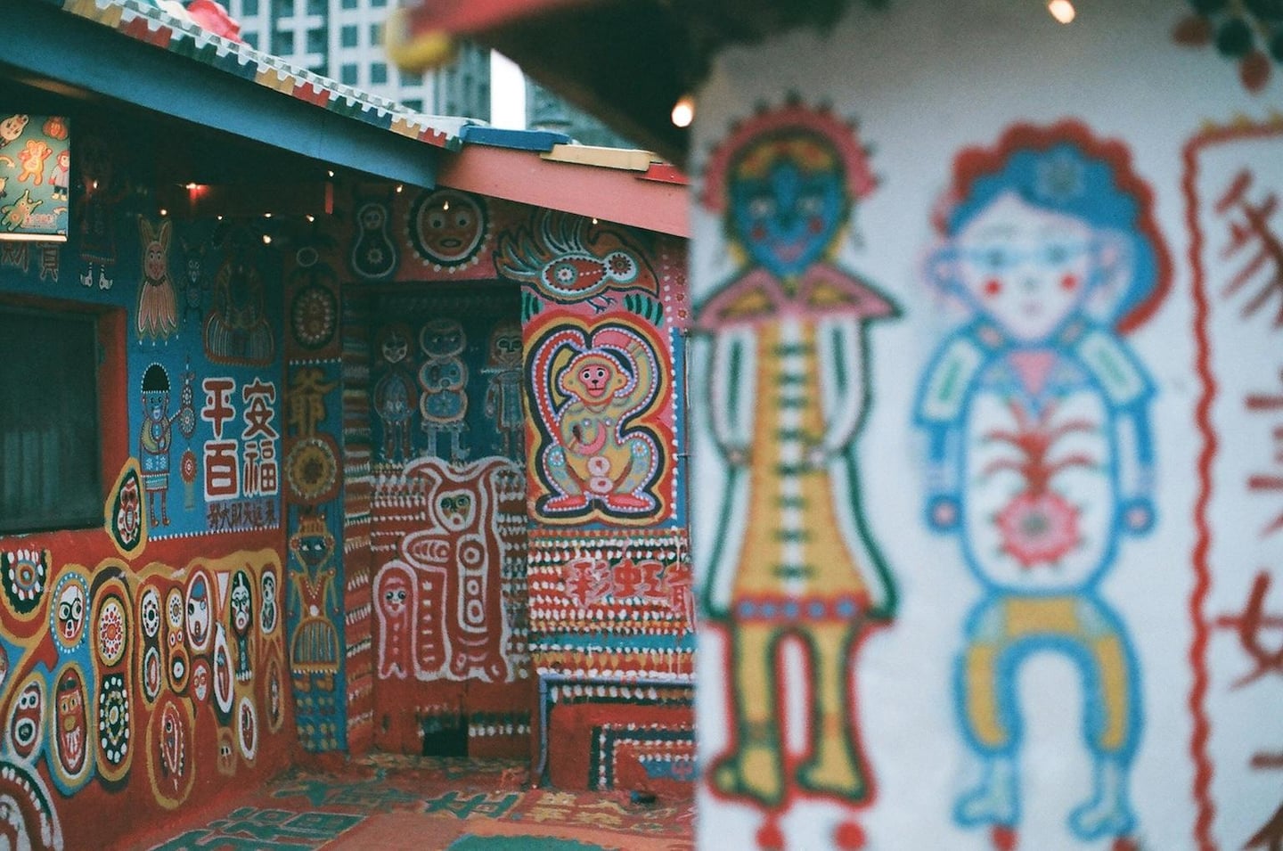 대만 타이중 무지개 마을의 알록달록한 벽화가 그려진 건물 외벽과 흐릿하게 보이는 전경의 캐릭터 그림들